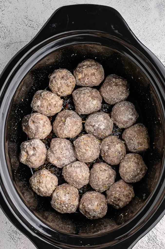 Frozen meatballs arranged in a single layer inside a black slow cooker